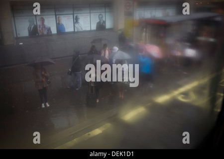 Vu à travers la fenêtre table-condensation, une foule de passagers utilisent les parasols à un arrêt d'autobus au cours de l'humidité, par temps sombre, au centre de Londres. Banque D'Images