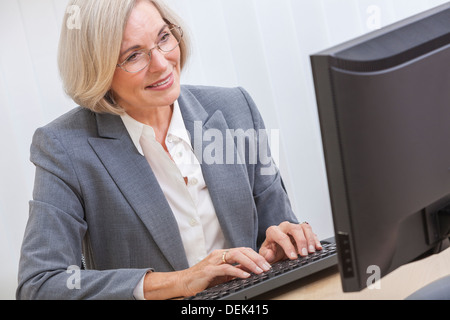 Senior woman la saisie à l'aide d'un ordinateur à la maison ou dans un bureau Banque D'Images