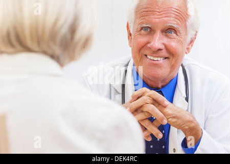 Un médecin homme assis à un bureau dans un bureau portant une chemise, cravate et parler aux personnes âgées stéthoscope female patient Banque D'Images