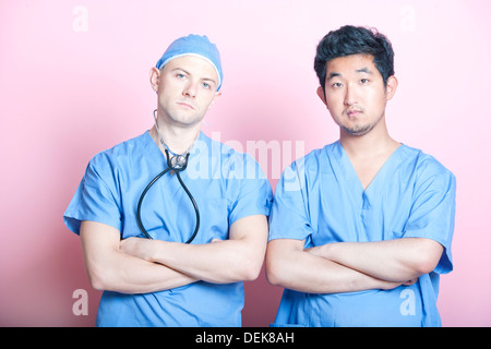 Portrait de deux chirurgiens mâle debout avec les bras croisés sur fond rose Banque D'Images