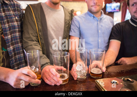 Quatre hommes en blanc s'alignent leurs verres à bière sur un bar dans un pub anglais à Londres, Royaume-Uni. Banque D'Images