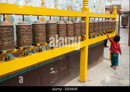 Un enfant tourne roues de prière aux côtés du plus grand Stupa du Népal à Katmandou, appelé Boudhanath Banque D'Images