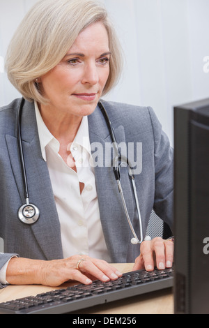 Une médecin assis à un bureau dans un bureau avec un ordinateur, en costume et stéthoscope Banque D'Images