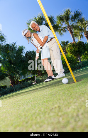 Happy senior man and woman couple ensemble jouer au golf et la mise sur un green, l'homme est l'enseignement de la femme comment mettre. Banque D'Images