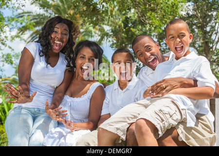 Happy black African American Family, deux parents, trois enfants, deux garçons une fille assis ensemble en dehors de rire s'amuser Banque D'Images