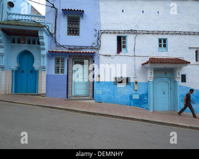 Homme marchant par les maisons peintes en bleu clair à Chefchaouen, Maroc Banque D'Images