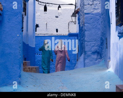 Deux femmes portant des vêtements traditionnels à pied dans une rue avec des murs peints en bleu à Chefchaouen, Maroc Banque D'Images