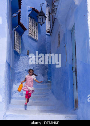 Jeune fille courir dans la rue avec des maisons peintes en bleu clair à Chefchaouen, Maroc Banque D'Images