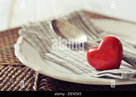 Plaque blanche, fourchette, couteau et coeur de pierre rouge sur fond de bois en osier libre. Focus sélectif. Banque D'Images