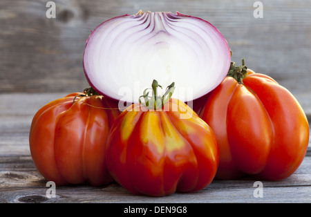 Trois Oxheart tomate et oignon rouge à partir de la moitié d'un marché hebdomadaire dans le sud de la France sur une vieille table en bois Banque D'Images