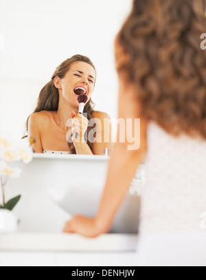 Happy young woman singing in brosse de maquillage dans la salle de bains Banque D'Images