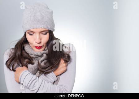 Jolie jeune femme en hiver la mode câlins à l'intérieur de son tricot jersey laineux gris, écharpe et cap sur une journée froide Banque D'Images