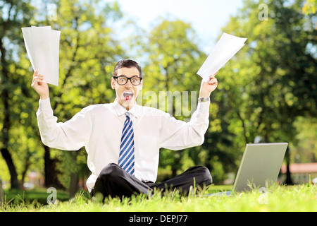 Inquiets businessman holding documents et criant assis sur une pelouse dans un parc Banque D'Images