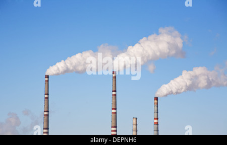 La fumée sort de l'industrie d'une cheminée contre le ciel bleu Banque D'Images