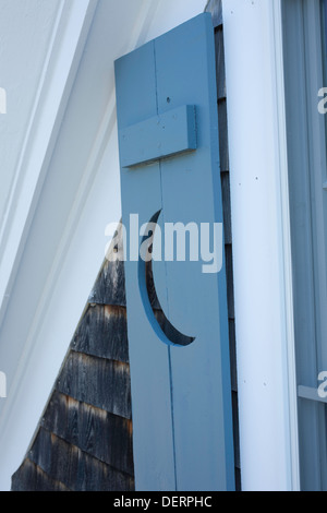 Une découpe croissant de lune décore un obturateur sur une fenêtre d'accueil de Cape Cod. Remarque d'évitement du bardeau cèdre typique derrière. Banque D'Images