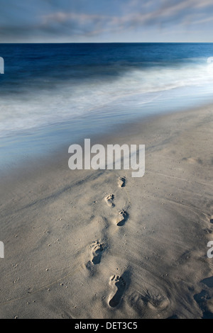 Des empreintes de pas dans le sable et flous, les vagues de l'océan avec nuages en mouvement Banque D'Images