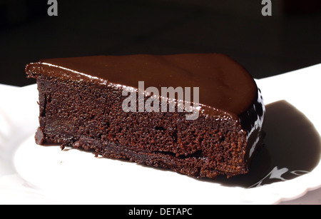 Une seule tranche de gâteau au chocolat noir maison avec ganache au chocolat, servi sur une assiette blanche. Banque D'Images