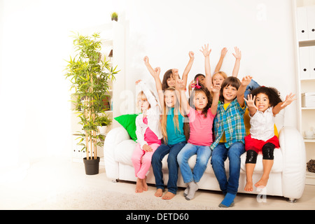 Groupe de huit professionnels peu 5-6 ans les enfants, garçons et filles, noirs, asiatiques et caucasiennes assis sur l'entraîneur à mains levées avec des visages heureux et Banque D'Images