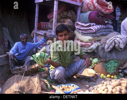 Jeune garçon vendant des légumes sur la rue pendant que les parents (couple) à la recherche sur en arrière-plan. Jaipur, Inde Banque D'Images