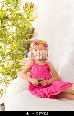 Petite fille de cinq ans avec une sourire wearing wreath text ses amis sur le réseau social assis sur le coach dans la salle de séjour Banque D'Images