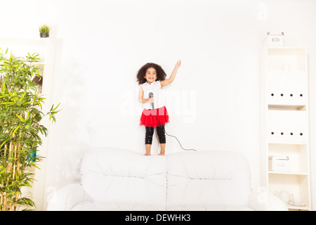 Jolie petite africaine noire fille de trois ans avec microphone d'effectuer debout sur le canapé