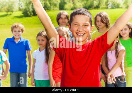 Fermer portrait of happy Asian boy with a levé les mains et très heureux d'expression. Ses amis et de l'équipe debout sur l'arrière-plan. Banque D'Images