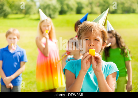 Beau garçon soufflant sifflent en corne torsadée parti avec beaucoup d'enfants sur l'arrière-plan Banque D'Images