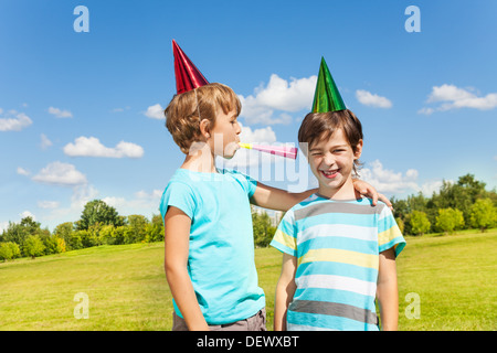 Deux garçons sur d'anniversaire s'amusant avec soufflant dans crécelle fort unis dans l'park Banque D'Images