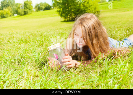 Portrait of happy fille avec de longs cheveux noirs 8 ans portant sur l'herbe vieux pot tenir debout avec papillon dans le parc à l'été à la journée ensoleillée à l'insecte Banque D'Images