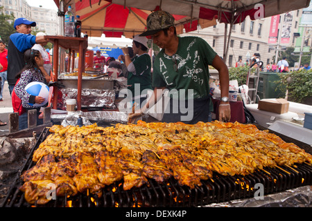 Griller les brochettes de poulet homme sur la grille du barbecue à un festival en plein air - USA Banque D'Images
