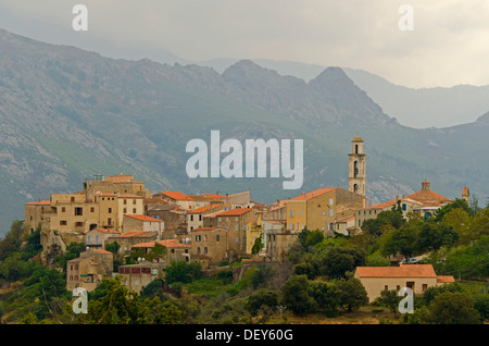 Le village de Montemaggiore dominée par la tour de son église en face de la silhouettes des montagnes escarpées de la Corse. Banque D'Images