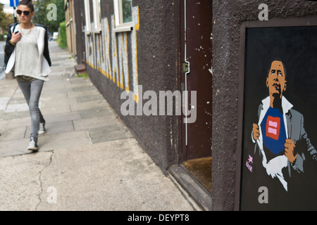 Une fille marche le long d'une rue, une image de graffiti le président Barack Obama a été peint sur le mur. Banque D'Images