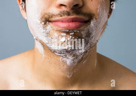 Close up sur le menton d'un jeune homme qu'il se prépare à se raser avec de la mousse et de l'eau Banque D'Images