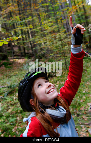 Porter un casque de cycliste fille pointant vers le haut, dans une forêt près de Grainau, Werdenfelser Land, Haute-Bavière, Bavière Banque D'Images