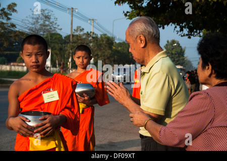 Matin l'aumône ronde, vieil homme accueil de jeunes moines bouddhistes d'un monastère, bols mendicité holding école Wai, traditionnel Banque D'Images