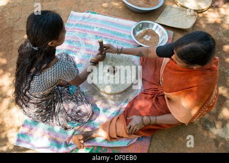 Les femmes village à l'aide de meules pierres pour moudre le mil rouge / Graines Graines Ragi Ragi en farine. L'Andhra Pradesh. L'Inde Banque D'Images