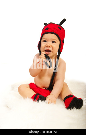 Cute baby boy in ladybug hat assis sur une couverture de fourrure contre fond blanc Banque D'Images