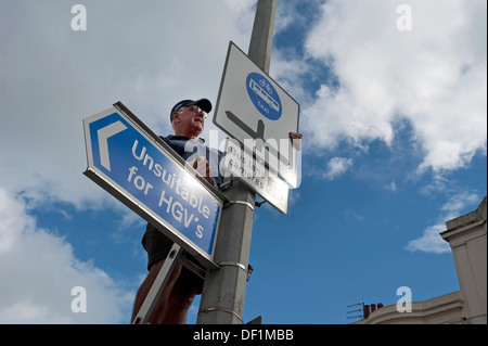 Un travailleur de la Voirie installe un Bus Lane, Taxis et cycles seulement signer plus un 'impropres pour les poids lourds" panneau d'avertissement sur un lampadaire. Banque D'Images