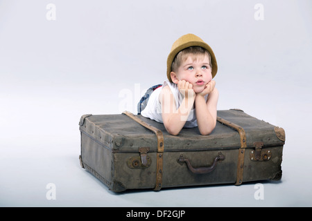 Thoughtful cute boy lying on the suitcase Banque D'Images