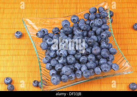 Bleuets frais dans un verre transparent plaque sur fond orange Banque D'Images