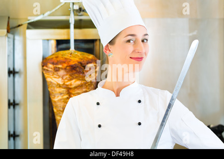 Döner Kebab - vendeur amical dans un restaurant fast food turc, avec un couteau en face de brochette Banque D'Images