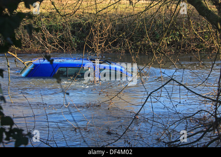 Une petite voiture bleue piégés et partiellement immergé dans un courant rapide de la rivière gonflée. Banque D'Images