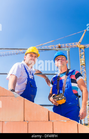 Deux fiers travailleurs du chantier ou maçons debout sur le projet de la maison à l'aide d'une télécommande de grue Banque D'Images