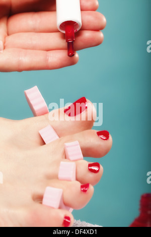 L'application de la pédicure pied femme pieds avec des ongles rouge rose dans les séparateurs d'orteil fond bleu Banque D'Images