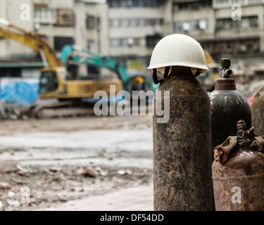 Casque sur une bouteille de gaz sur un chantier avec des gravats et des camions de démolition Banque D'Images
