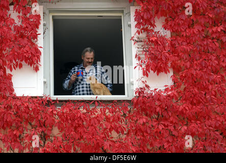 Walter Habeler et son chat Mex profitez de l'atmosphère à une fenêtre ouverte encadrée de feuilles rouges à Titisee-Neustadt, Allemagne, 28 septembre 2013. Photo : PATRICK SEEGER Banque D'Images