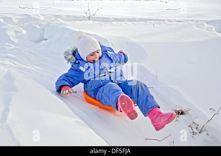 Petite fille sur un traîneau glissant sur une colline dans la neige en hiver Banque D'Images