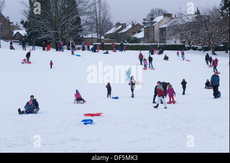Beaucoup de personnes (adultes et enfants) ayant plaisir en famille en hiver la neige, de la luge en bas de la colline dans le parc - Riverside Gardens, Ilkley, Yorkshire, Angleterre, Royaume-Uni. Banque D'Images