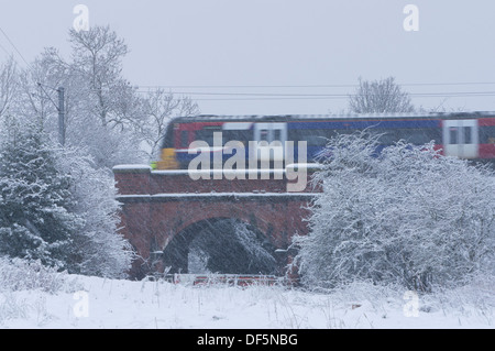 La neige tombe et est train de voyageurs locaux crossing bridge, le long de la ligne de Wharfedale on snowy winter day - Baildon, West Yorkshire, Angleterre, Royaume-Uni. Banque D'Images