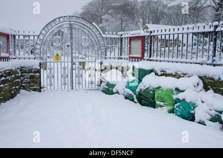 Sacs de déchets de jardin décoratif empilés par les portes en fer forgé sur journée d'hiver enneigée - entrée de Cliffe Hall jardins communautaires, Baildon, UK. Banque D'Images